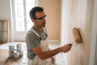 Artisan peintre professionnel appliquant de la peinture beige sur un mur intérieur dans un appartement en rénovation à Paris