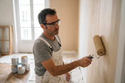 Artisan peintre professionnel appliquant de la peinture beige sur un mur intérieur dans un appartement en rénovation à Paris