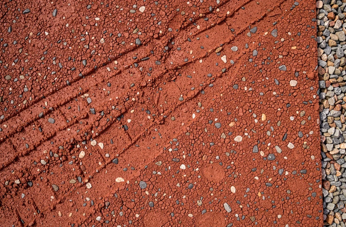 Gros plan sur la texture d'enrobé rouge, détail des granulats et de la surface bitumineuse colorée d'une allée